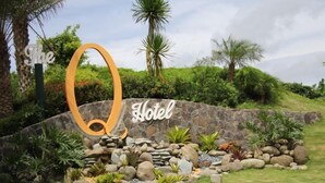 L’entrée d’un hôtel, marquée par un grand panneau en forme de « O », est entourée d’un jardin aménagé avec des rochers et des plantes.