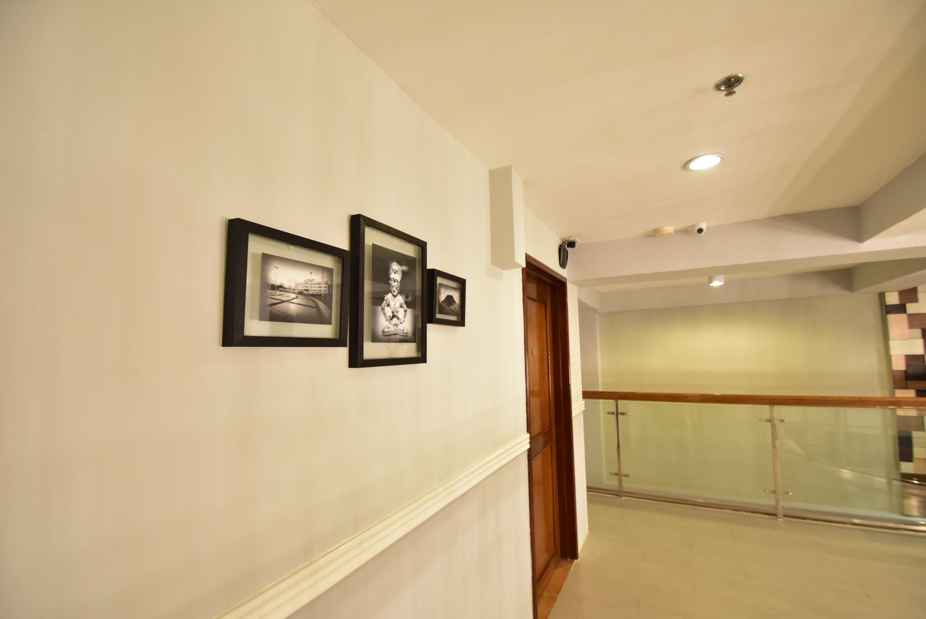 A hallway with framed pictures on the wall, a wooden door, and a glass railing in the background.