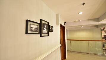 A hallway with framed pictures on the wall, a wooden door, and a glass railing in the background.