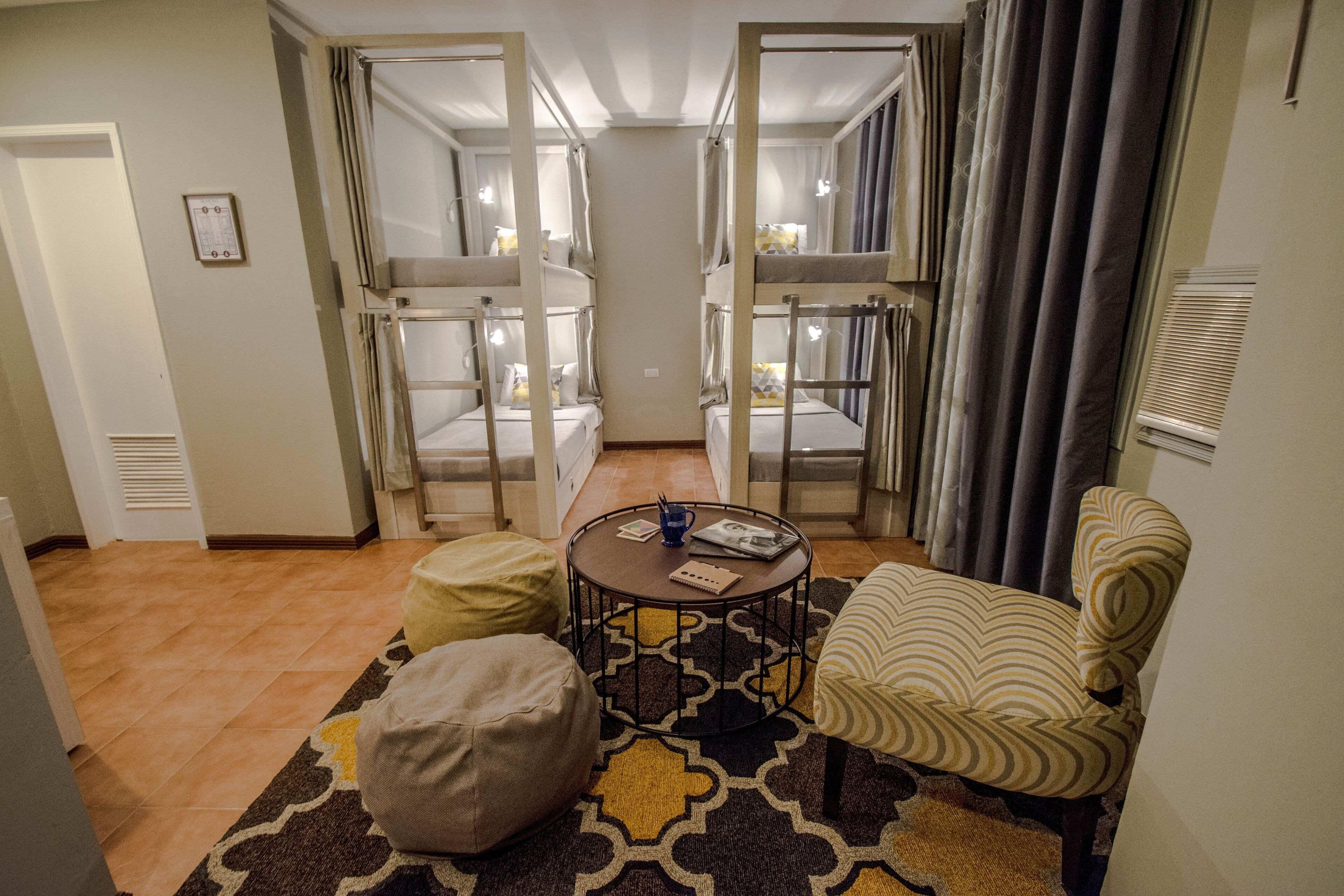 A hotel room with bunk beds, a round coffee table, a patterned rug, and a striped armchair.