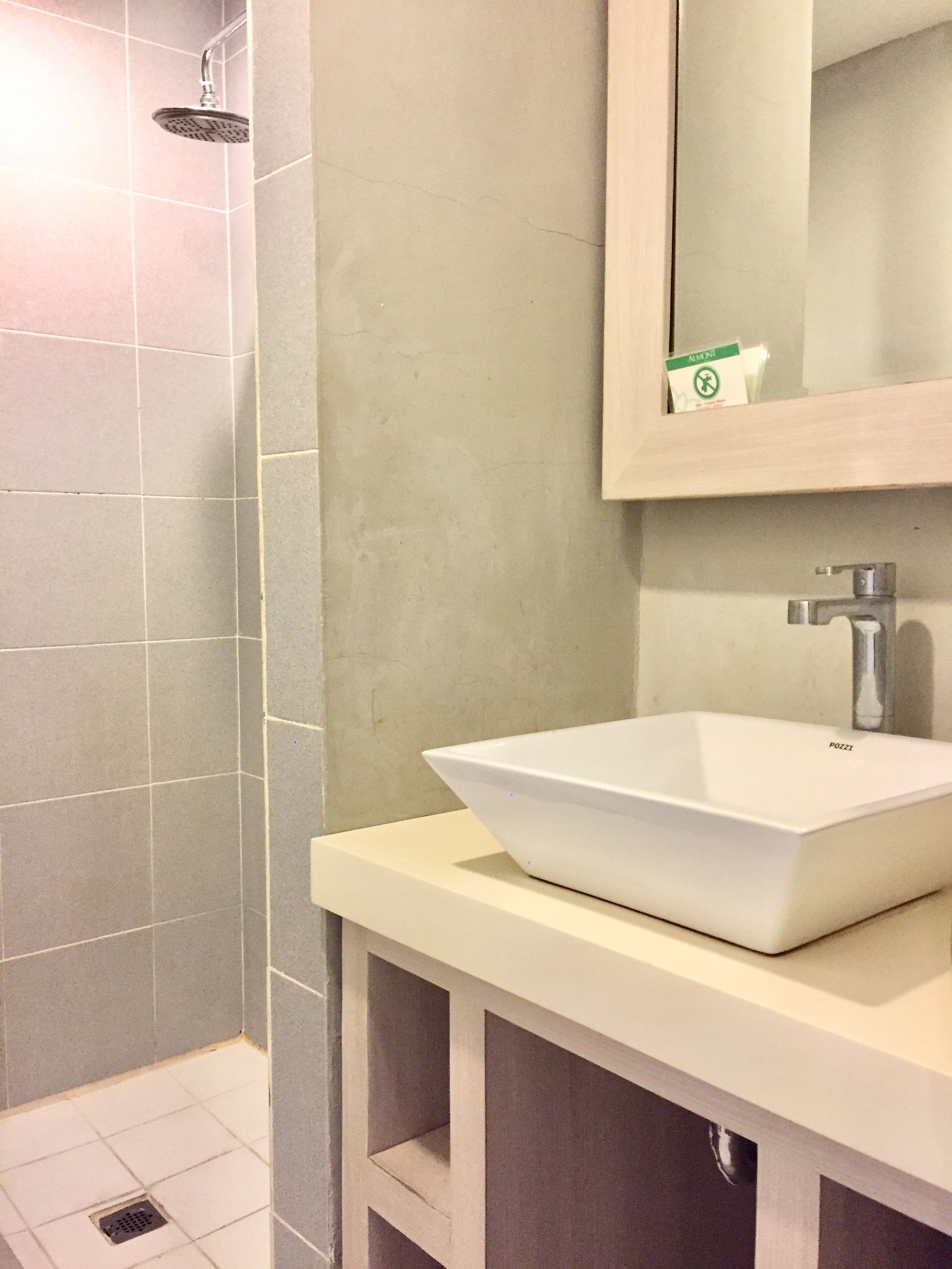 Een badkamer met een witte wastafel, een handdouche en een spiegel met een groen bordje.