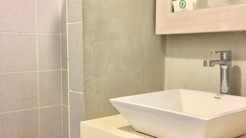 Een badkamer met een witte wastafel, een handdouche en een spiegel met een groen bordje.