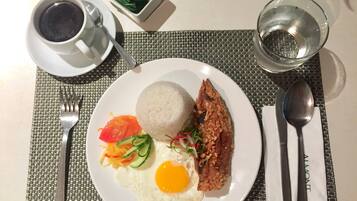 Un plato con arroz, un huevo frito, carne frita y verduras, una taza de café y un vaso de agua sobre una mesa.