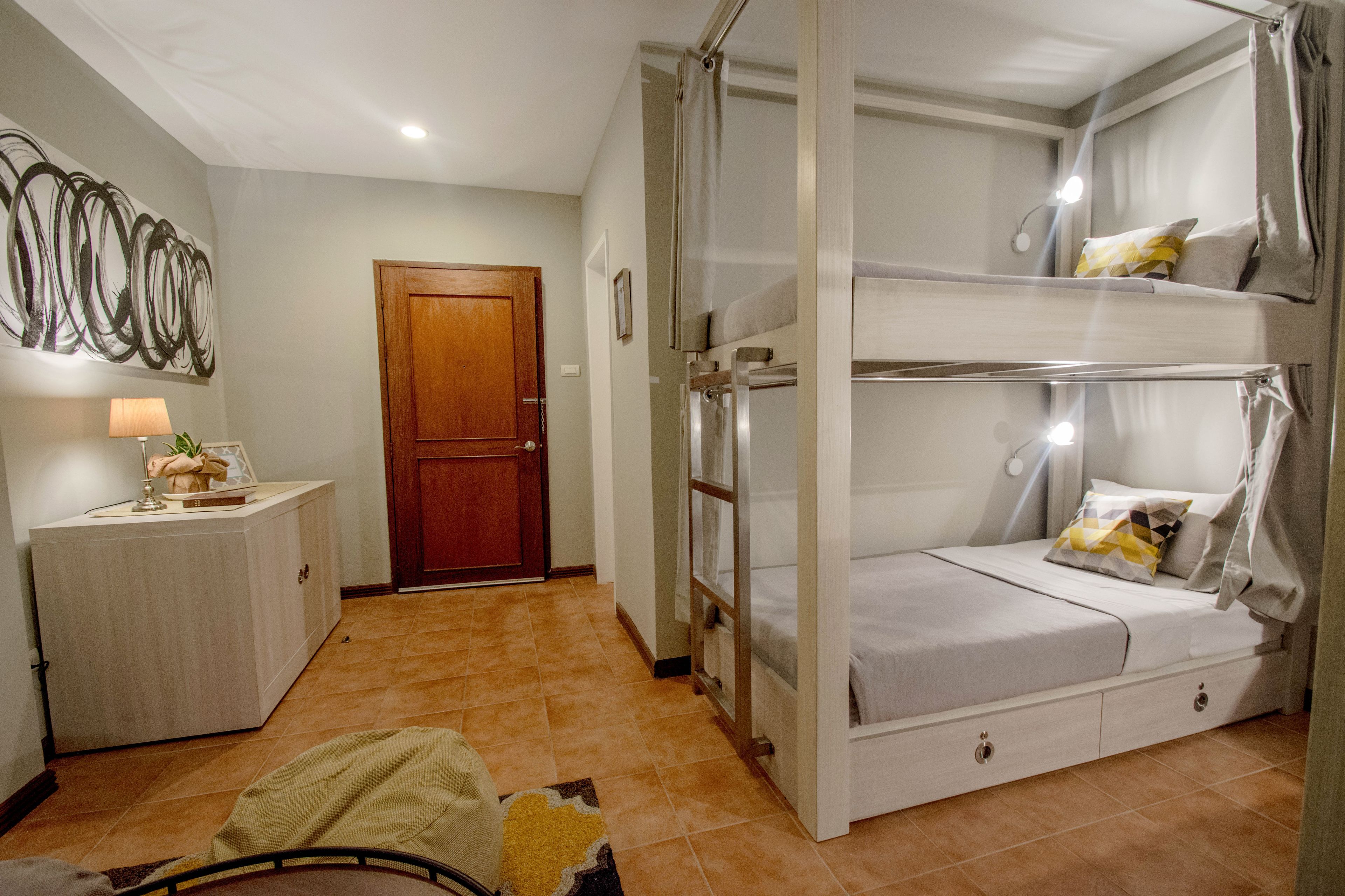 A room with a bunk bed, a bedside table with a lamp, a door, and a wall with abstract art.