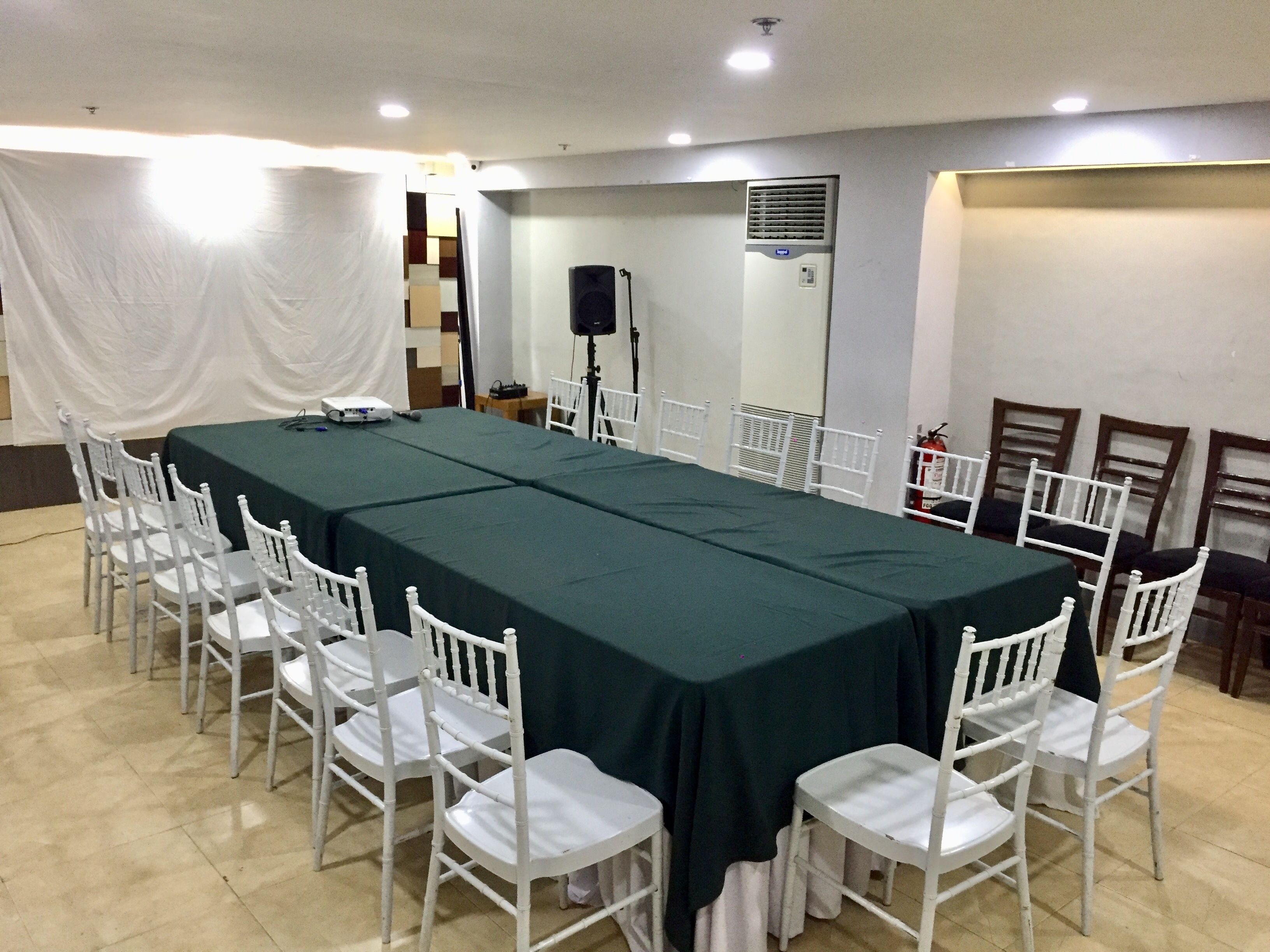 A conference room with a long table, white chairs, a speaker, and a fire extinguisher.
