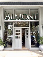 El exterior del Hotel Almont City con un gran letrero sobre la entrada, ventanas amplias y una puerta con un escalón que la precede.