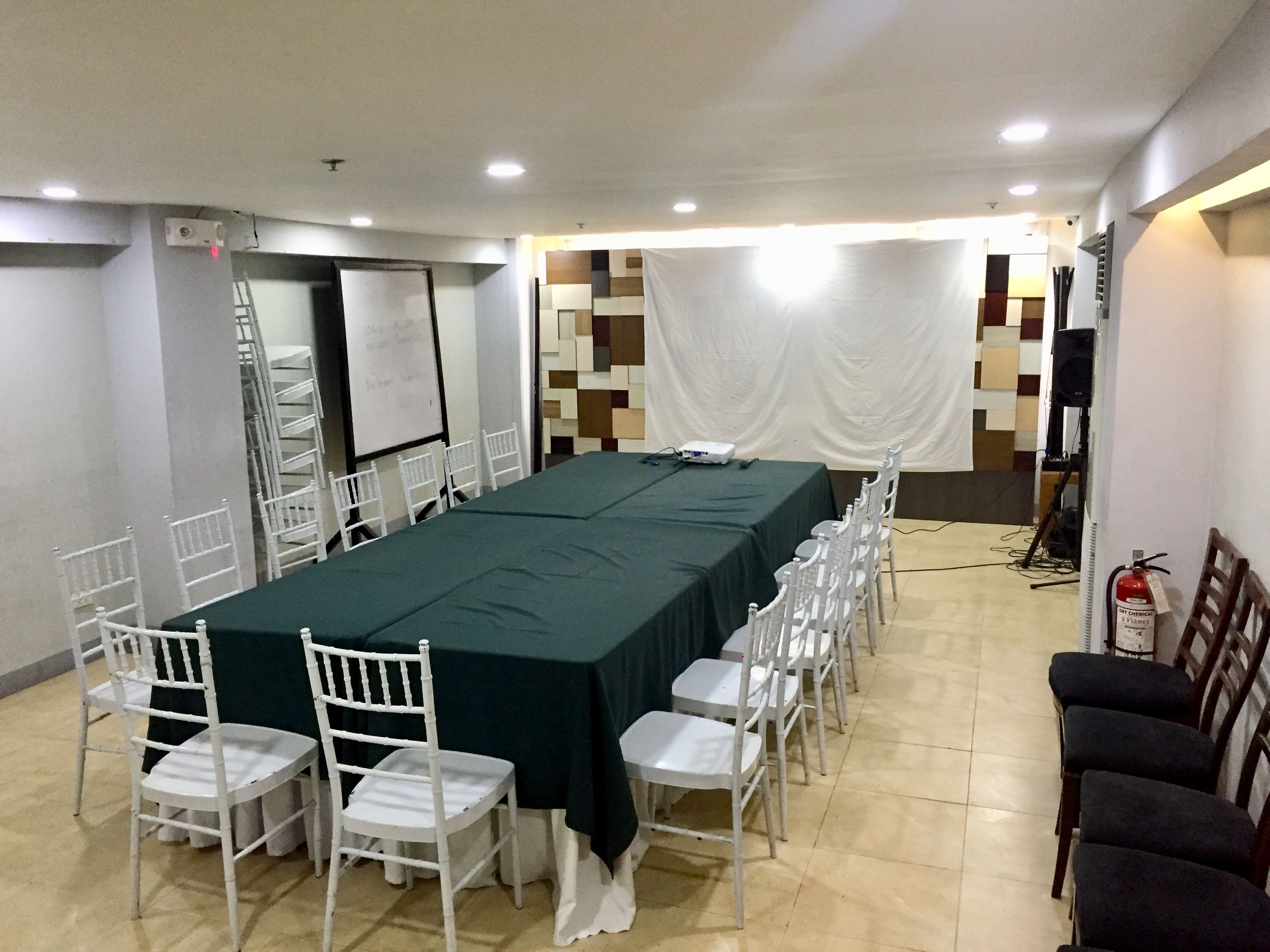 Una sala de conferencias con una larga mesa, sillas blancas, una pizarra y un proyector.