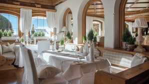 Uma sala de jantar com toalhas brancas, lustres e vista para as montanhas.