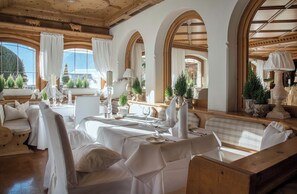 Une salle Ă manger avec des nappes blanches, des lustres et une vue sur les montagnes.