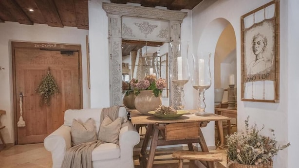 Um quarto acolhedor com porta de madeira, um sofá branco, uma mesa de madeira e um espelho com detalhes florais.