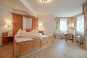 Ein Zimmer mit einem hölzernen Himmelbett, zwei Nachttischlampen, einem Sessel, einem kleinen Tisch und einem Fenster mit Vorhängen.