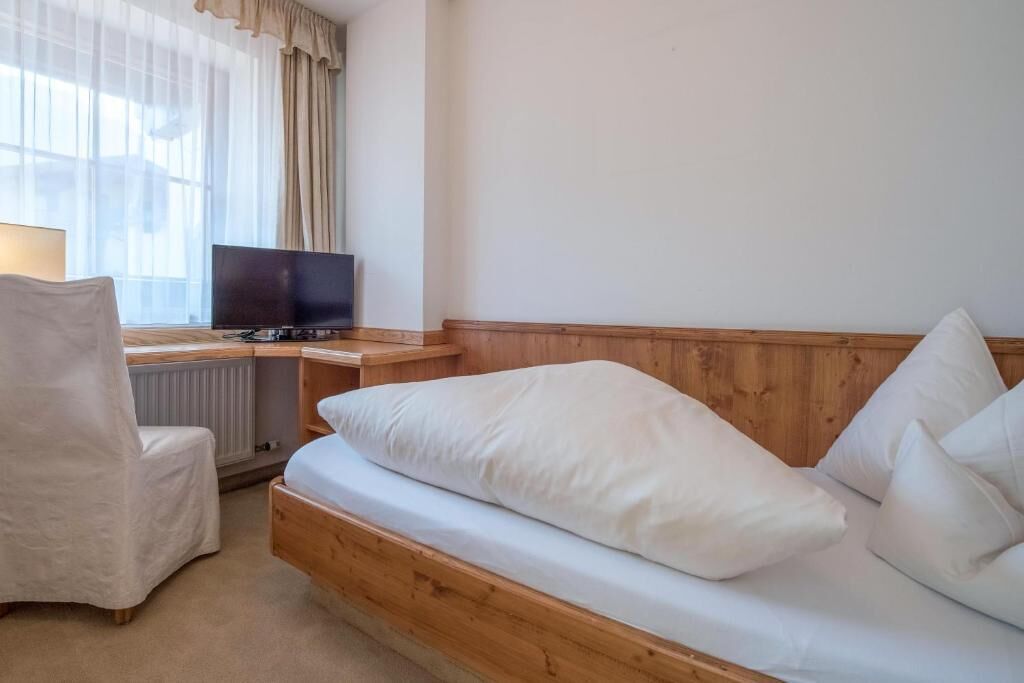 Ein Zimmer mit einem Bett, einem Sessel, einem Schreibtisch mit Fernseher und einem Fenster mit Vorhängen.