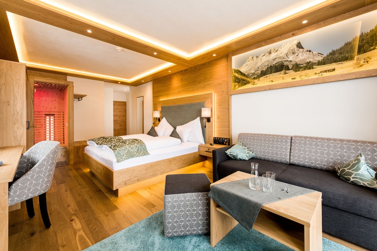 A modern hotel room with a bed, sofa, and a desk.