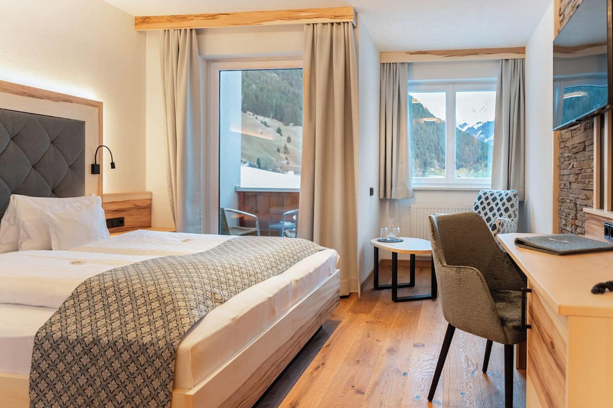 A hotel room with a bed, a desk, a chair, and a view of a mountainous landscape.