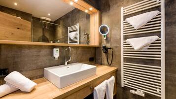 Un baño moderno con tocador de madera, lavabo blanco, cabina de ducha de vidrio y toallero con varias toallas.