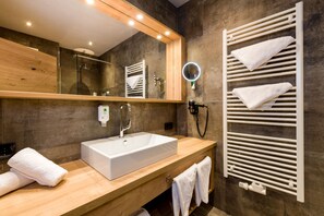 Un baño moderno con tocador de madera, lavabo blanco, cabina de ducha de vidrio y toallero con varias toallas.