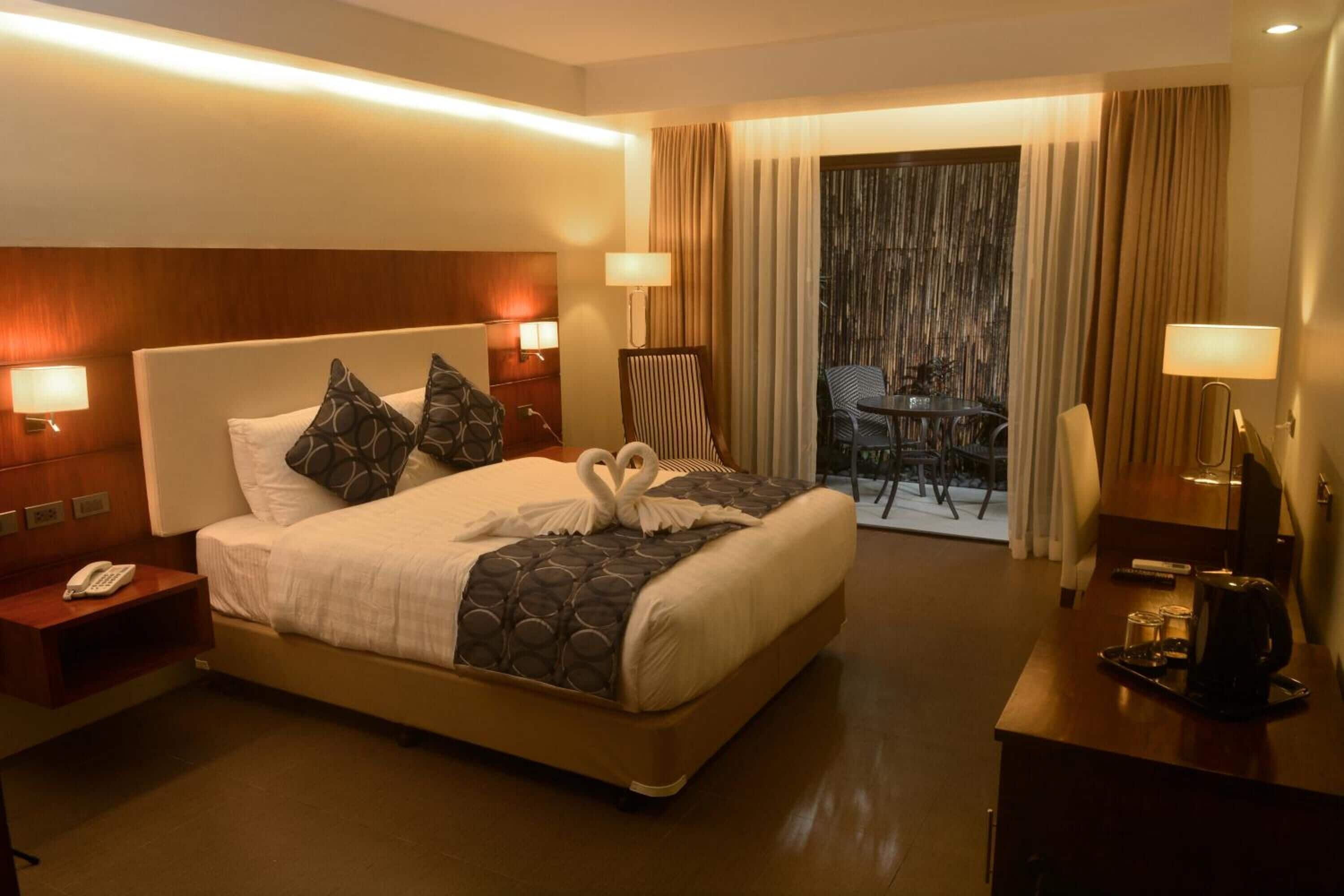 Une chambre d’hôtel avec un grand lit, deux lampes de chevet, un bureau avec une machine à café et une vue sur le balcon extérieur.