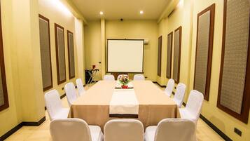 Un salón de conferencias con una larga mesa, sillas blancas y una pantalla para proyector.