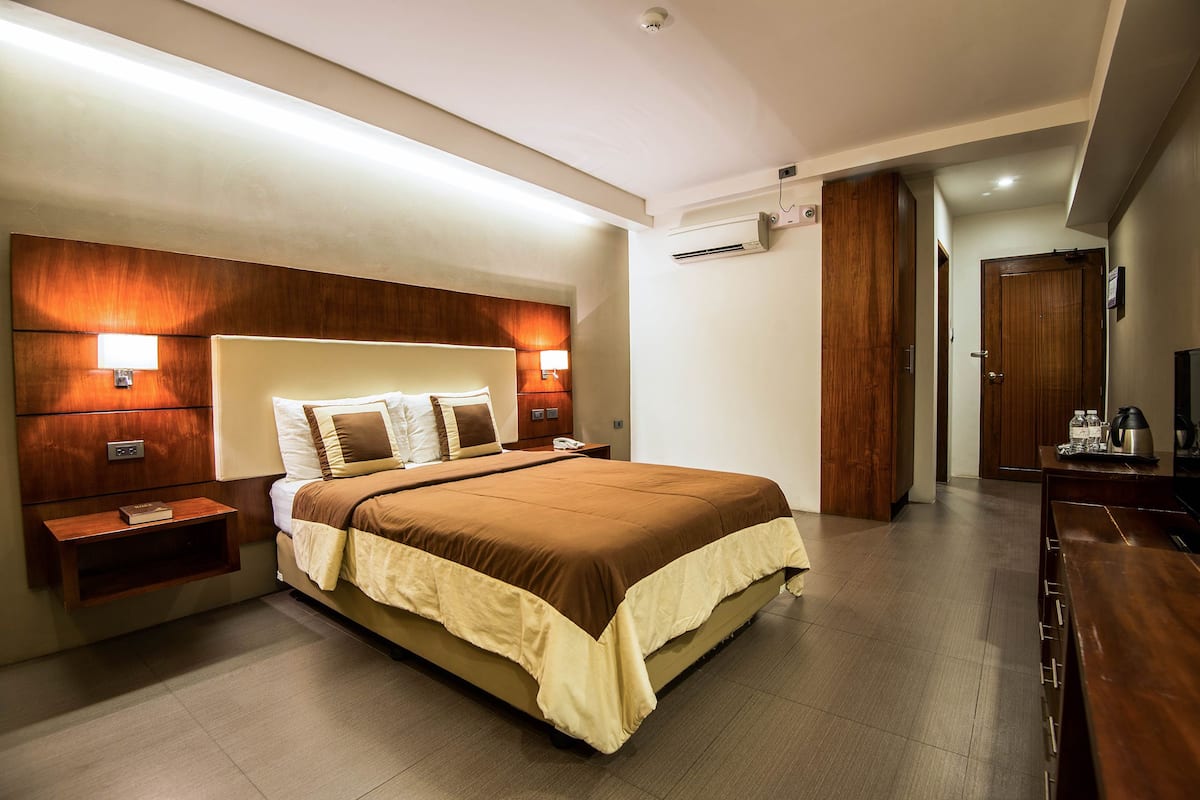 A modern hotel room with a large bed, bedside tables, a wardrobe, and a desk with a chair.