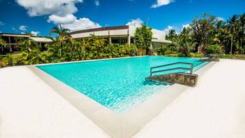 A clear blue pool with a stone border, surrounded by lush greenery and a modern building in the background.