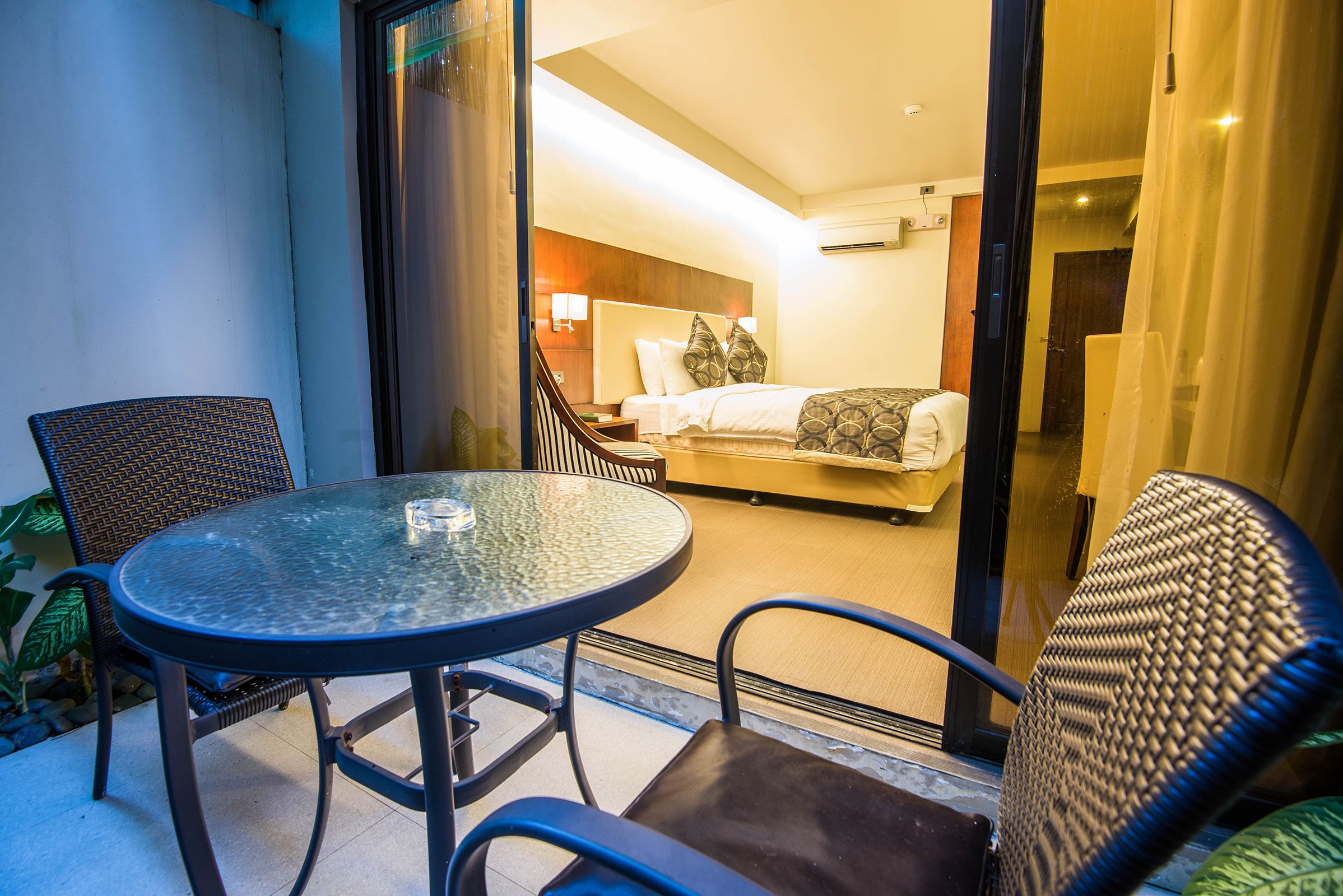 A hotel room with a bed, a glass table, and two chairs.