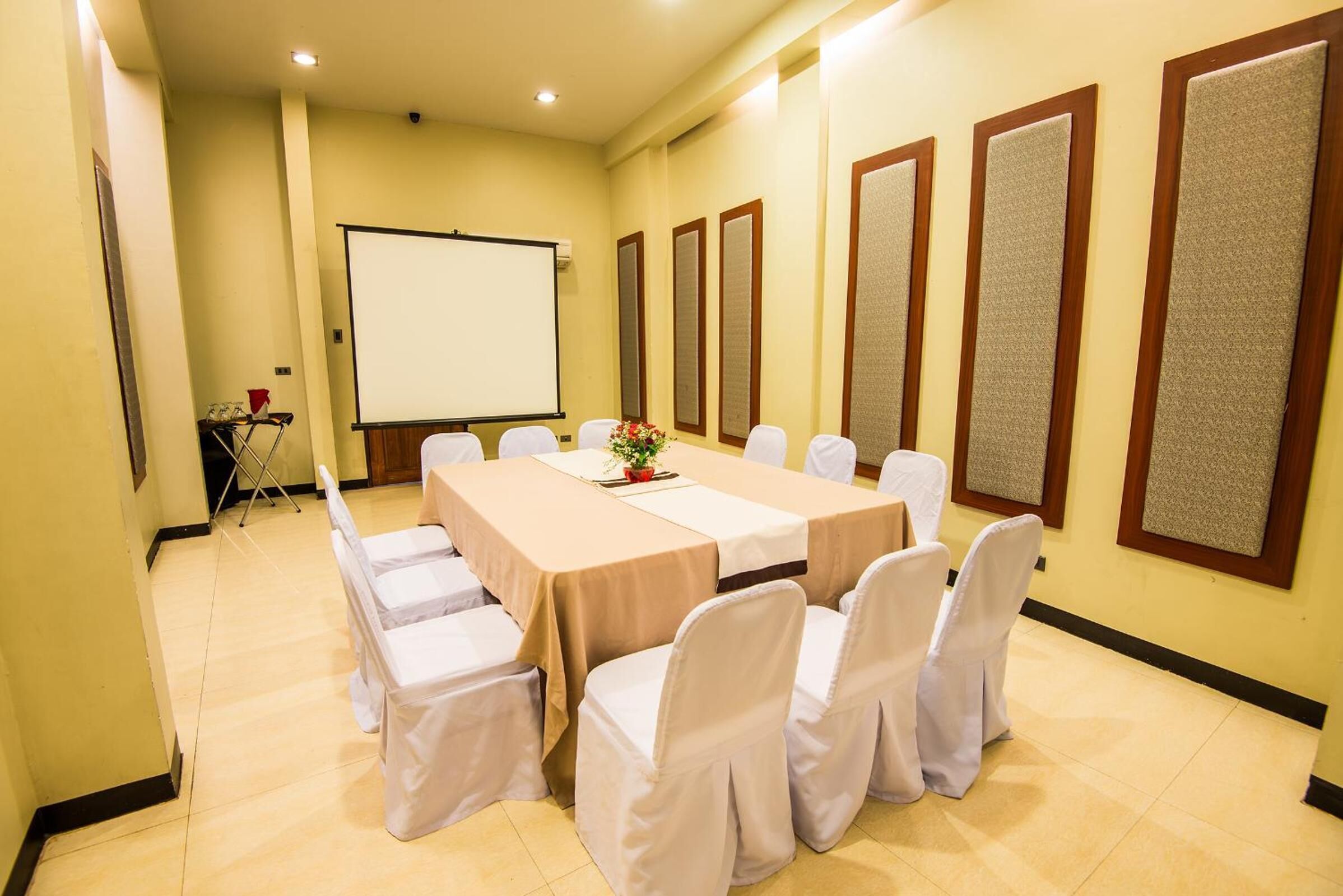 A conference room with a long table, white chairs, a projector screen, and soundproof panels on the walls.