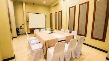 A conference room with a long table, white chairs, a projector screen, and soundproof panels on the walls.