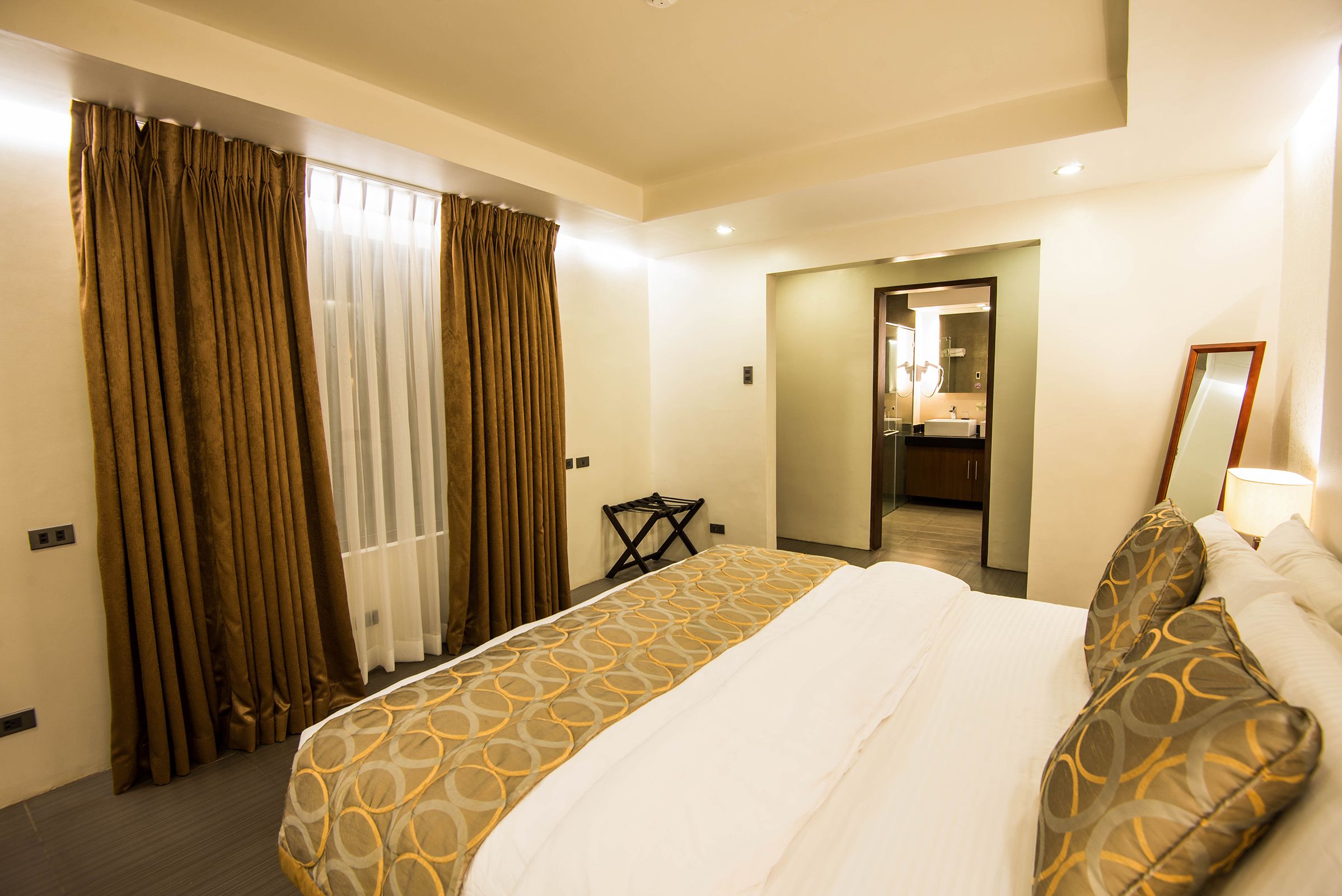 Une chambre d’hôtel avec un grand lit, des rideaux, une petite table et un miroir.