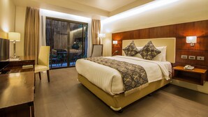 A hotel room with a large bed, a desk, a chair, a nightstand, and a view of the outdoors. - Ariana Hotel (Dipolog)