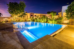 A nighttime swimming pool area with a clear pool, surrounding palm trees, and a building with multiple windows. - Ariana Hotel (Dipolog)
