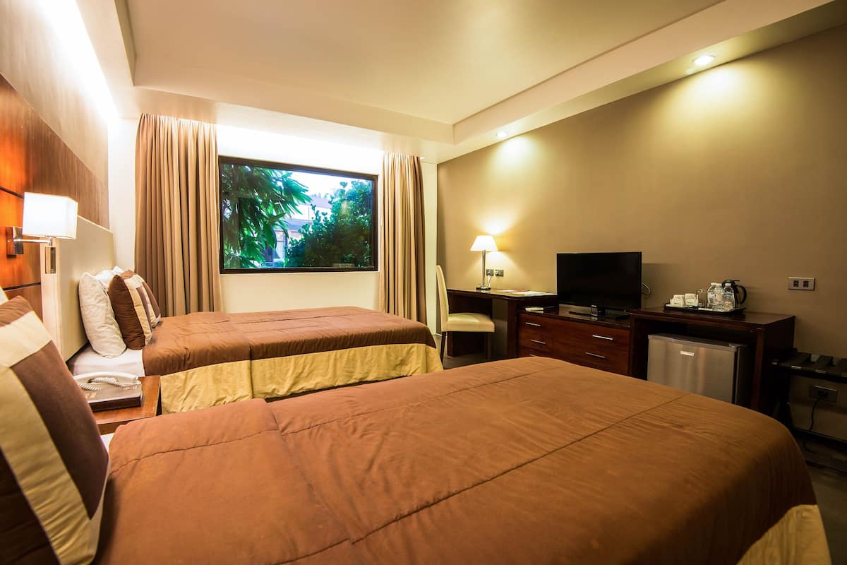 A hotel room with two beds, a desk, a television, and a small refrigerator.