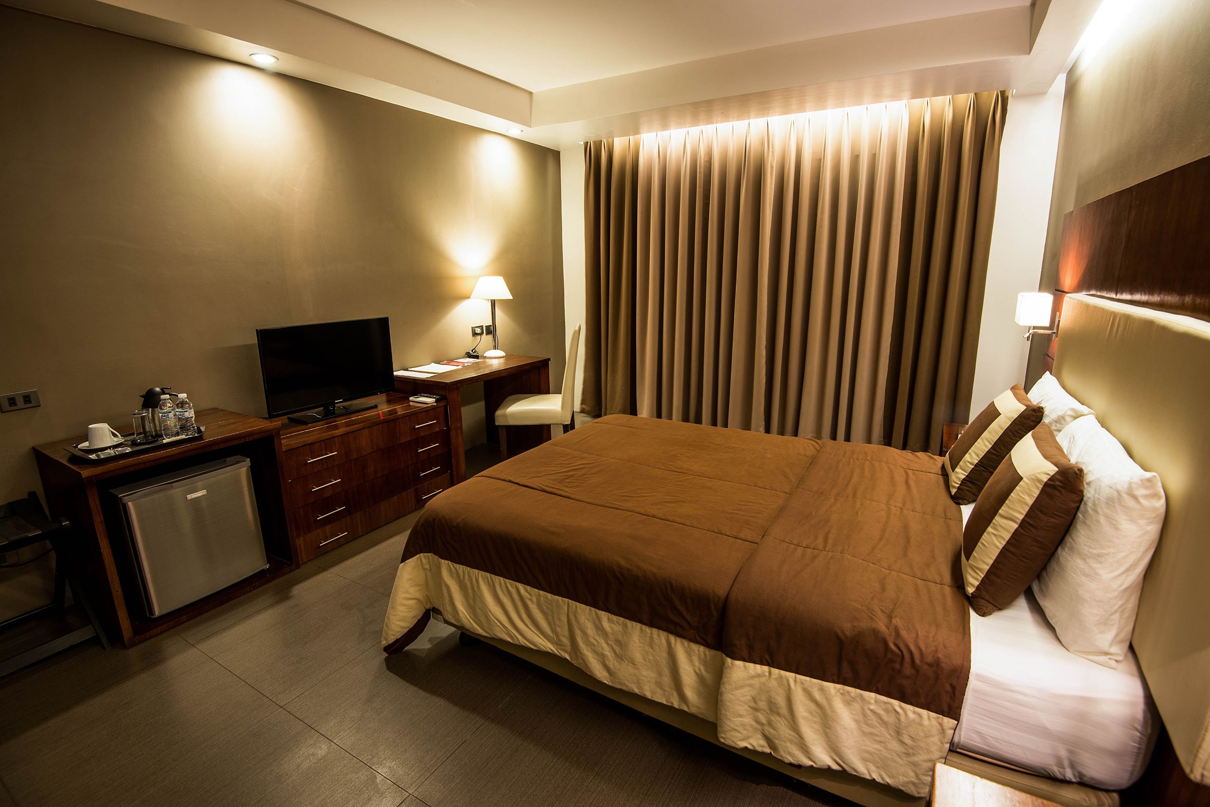 Habitación de hotel con cama, escritorio, televisión y minibar.
