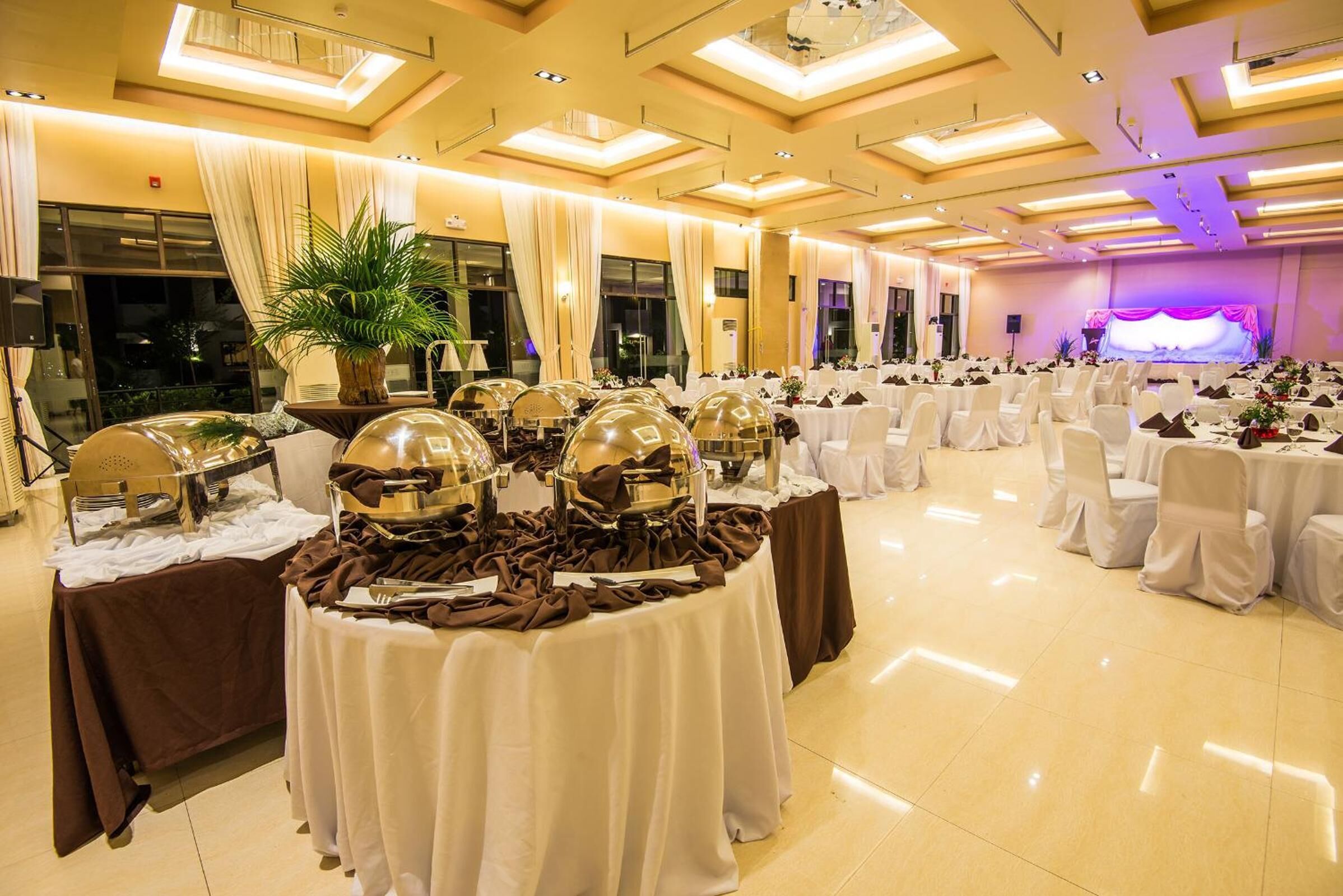 Un salón de banquetes con mesas redondas cubiertas con manteles blancos, dispuestas en filas.