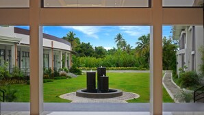 A modern building with a central courtyard featuring a circular water feature, surrounded by lush greenery and palm trees. - Ariana Hotel (Dipolog)