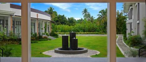 A modern building with a central courtyard featuring a circular water feature, surrounded by lush greenery and palm trees.