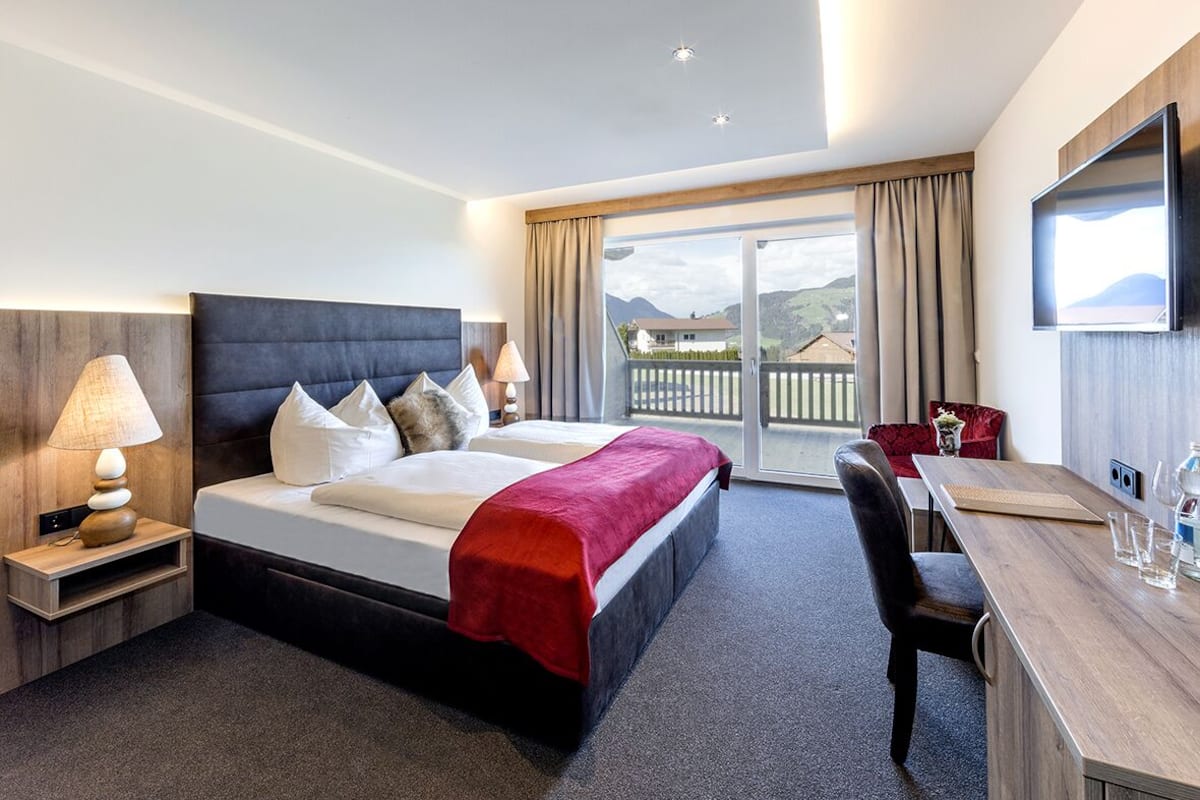 A hotel room with a bed, a desk, a chair, a TV, and a balcony with a view.