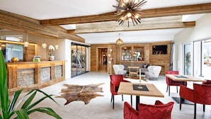A spacious room with wooden beams, a stone fireplace, and a large window. - Hotel Leamwirt (Hopfgarten im Brixental)