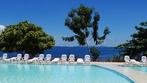 Ein Poolbereich mit weißen Liegestühlen und einem Tisch, mit Blick auf das klare, blaue Meer.