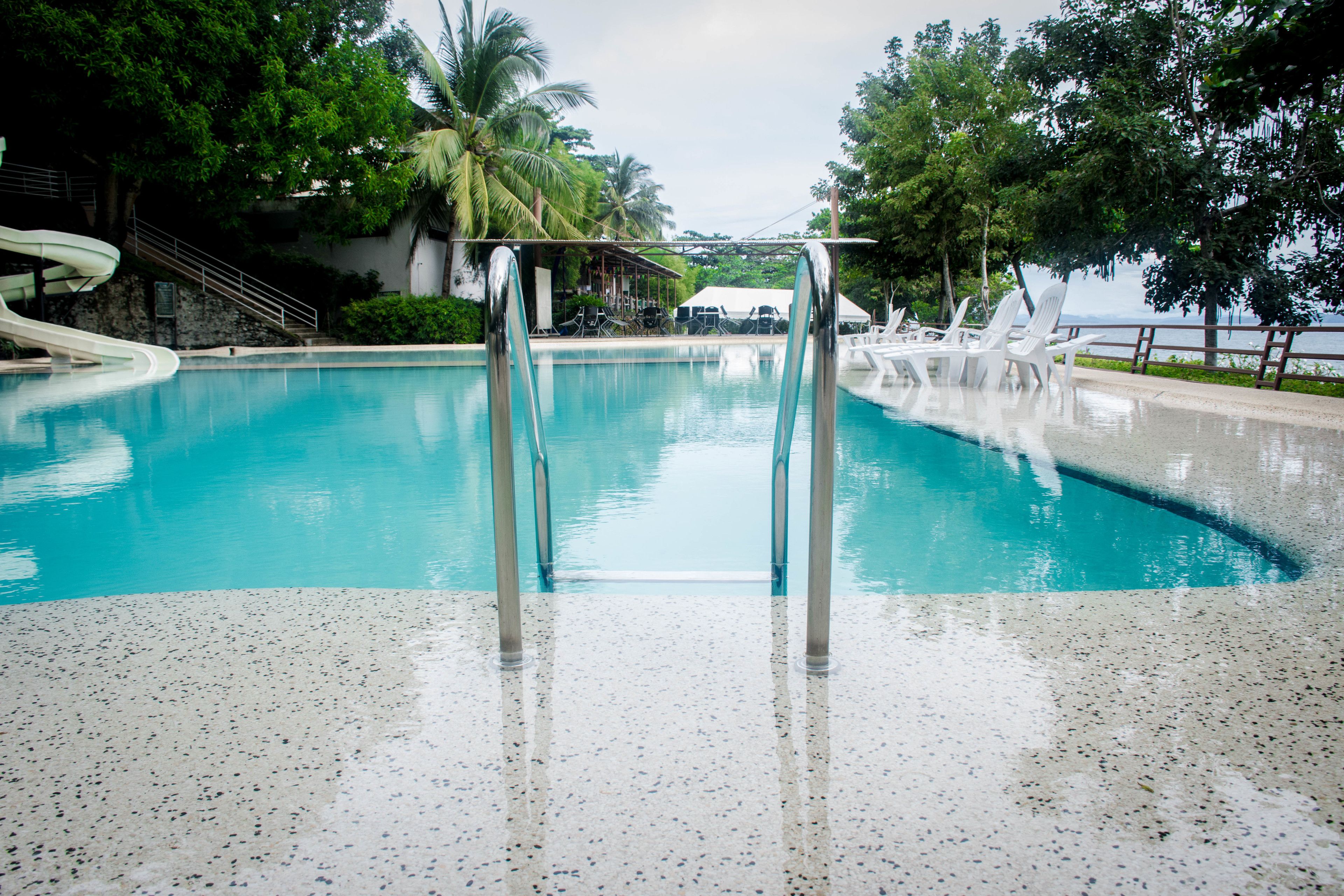 Una piscina con tobogán de agua, rodeada de árboles y vista al agua.