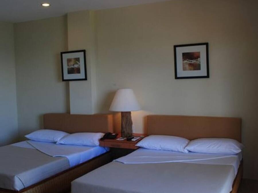 A hotel room with two beds, a nightstand, a lamp, and two framed pictures on the wall.