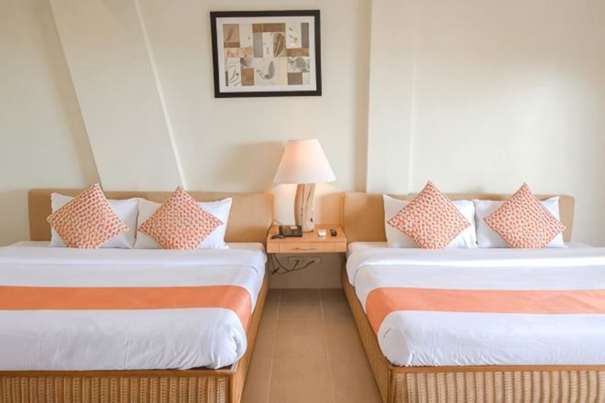 A hotel room with two beds, a nightstand, a lamp, and a framed picture on the wall.