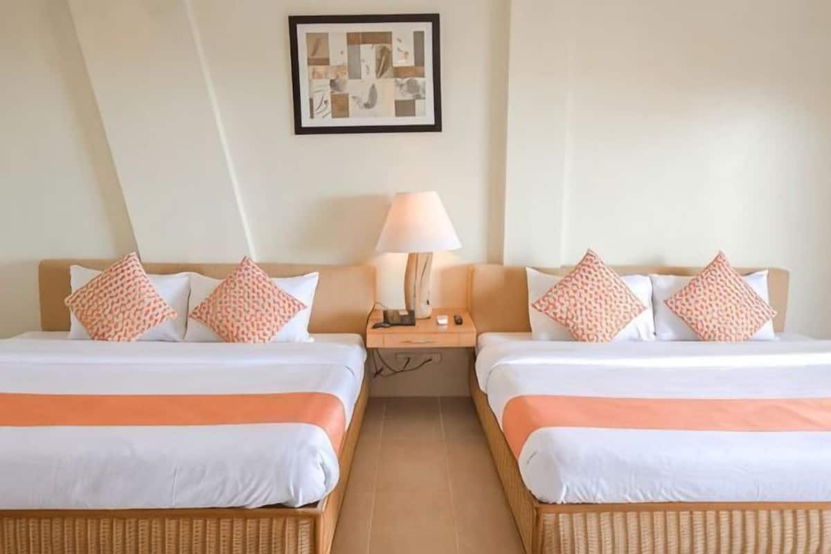 Quarto de hotel com duas camas, mesa de cabeceira, abajur e um quadro na parede.