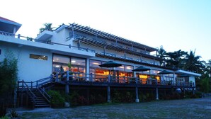 Ein zweistöckiges Gebäude mit überdachter Terrasse, einer Treppe zum oberen Stockwerk und Sitzgelegenheiten im Freien mit Sonnenschirmen.