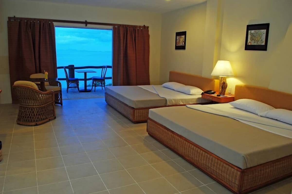 Quarto de hotel com duas camas, uma varanda com vista, uma mesa pequena e uma cadeira.