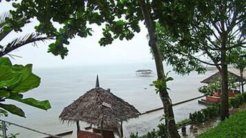 Une vue sur la côte, avec une construction à toit de chaume, un bateau sur l’eau et un bâtiment au toit rouge.