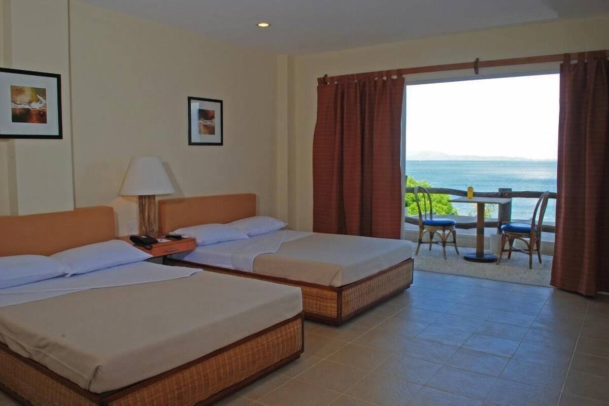 Quarto de hotel com duas camas, uma mesa com cadeiras e vista para o mar.