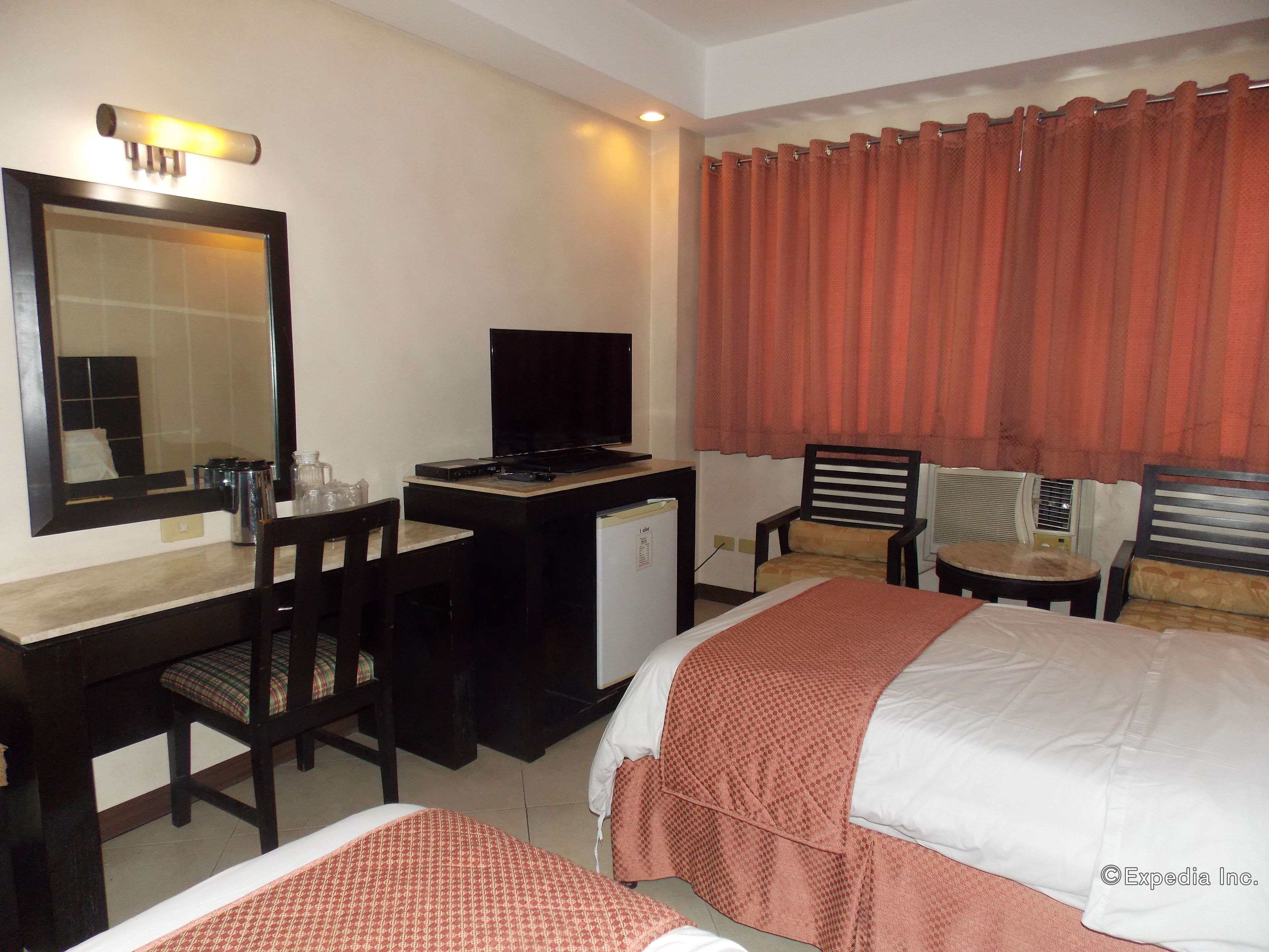 A hotel room with a bed, a desk with a computer, a chair, a television, and a window with curtains.