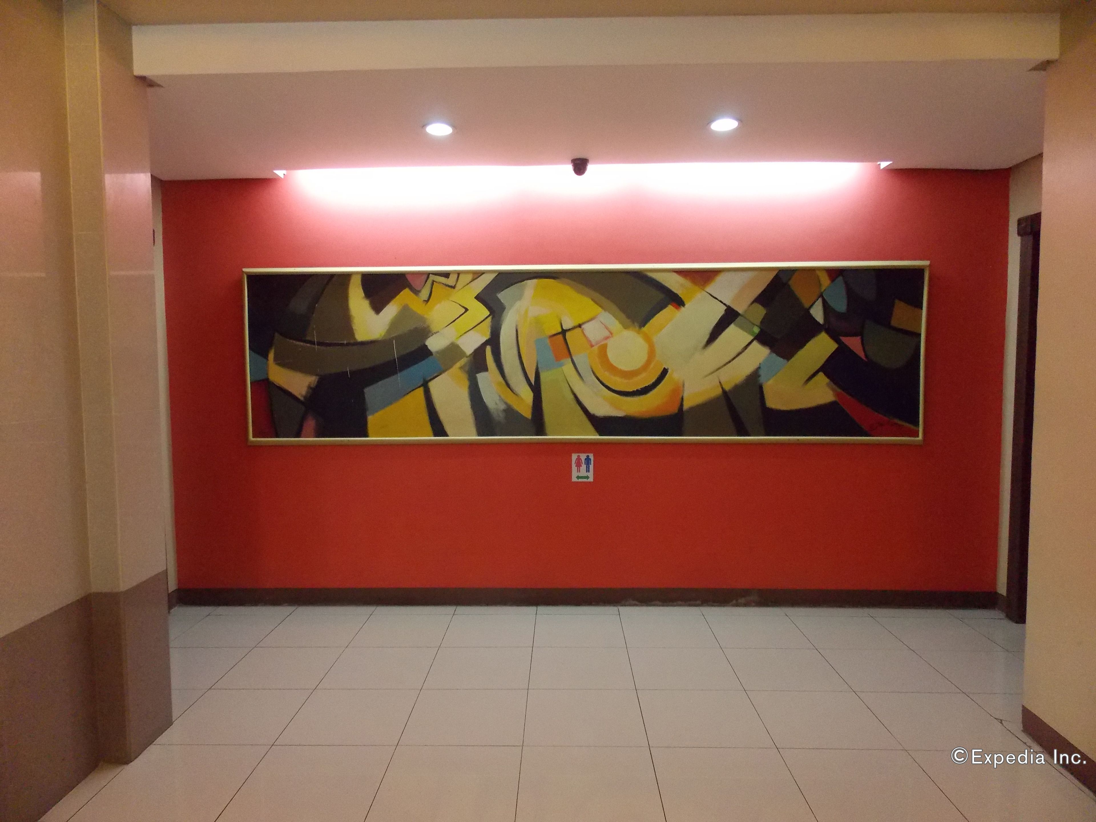 Un pasillo con un cuadro abstracto grande en la pared, suelo de baldosas y señal de salida de incendios.