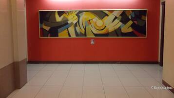 Un pasillo con un cuadro abstracto grande en la pared, suelo de baldosas y señal de salida de incendios.