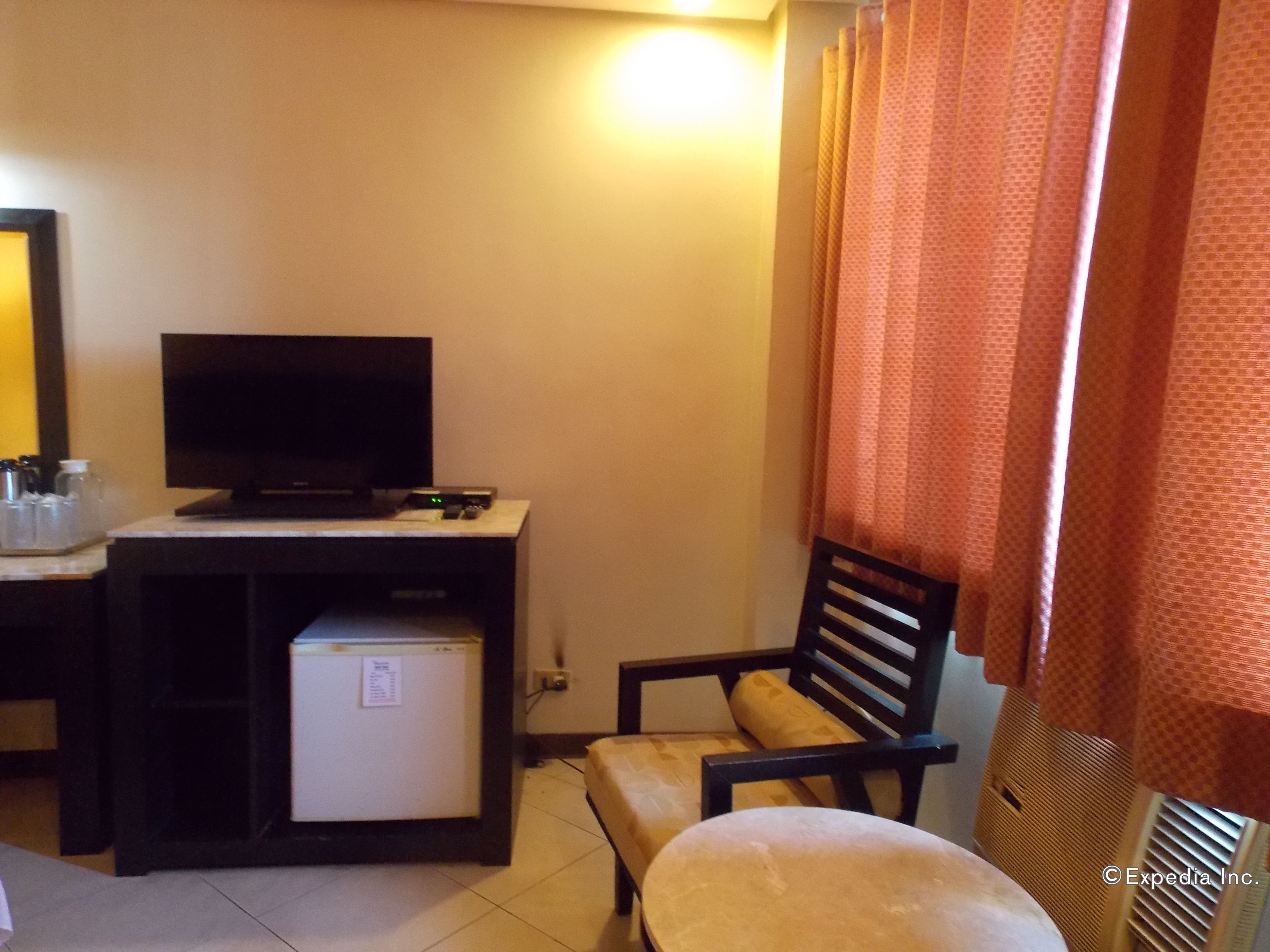 Una habitación de hotel compacta con televisión, un refrigerador pequeño, un escritorio y una silla.